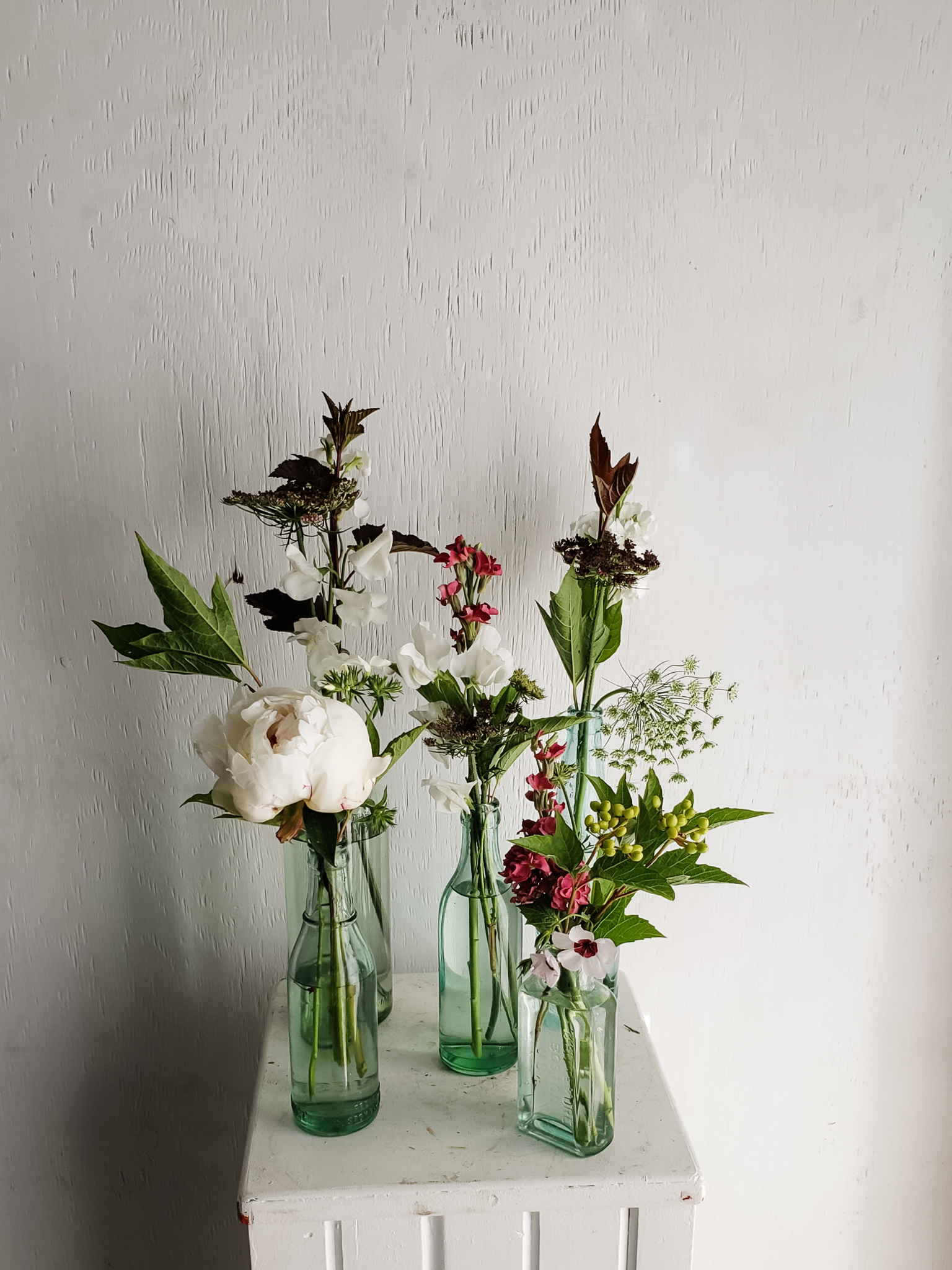 Designed green bottles of flowers for a wedding with white and pink country flowers.