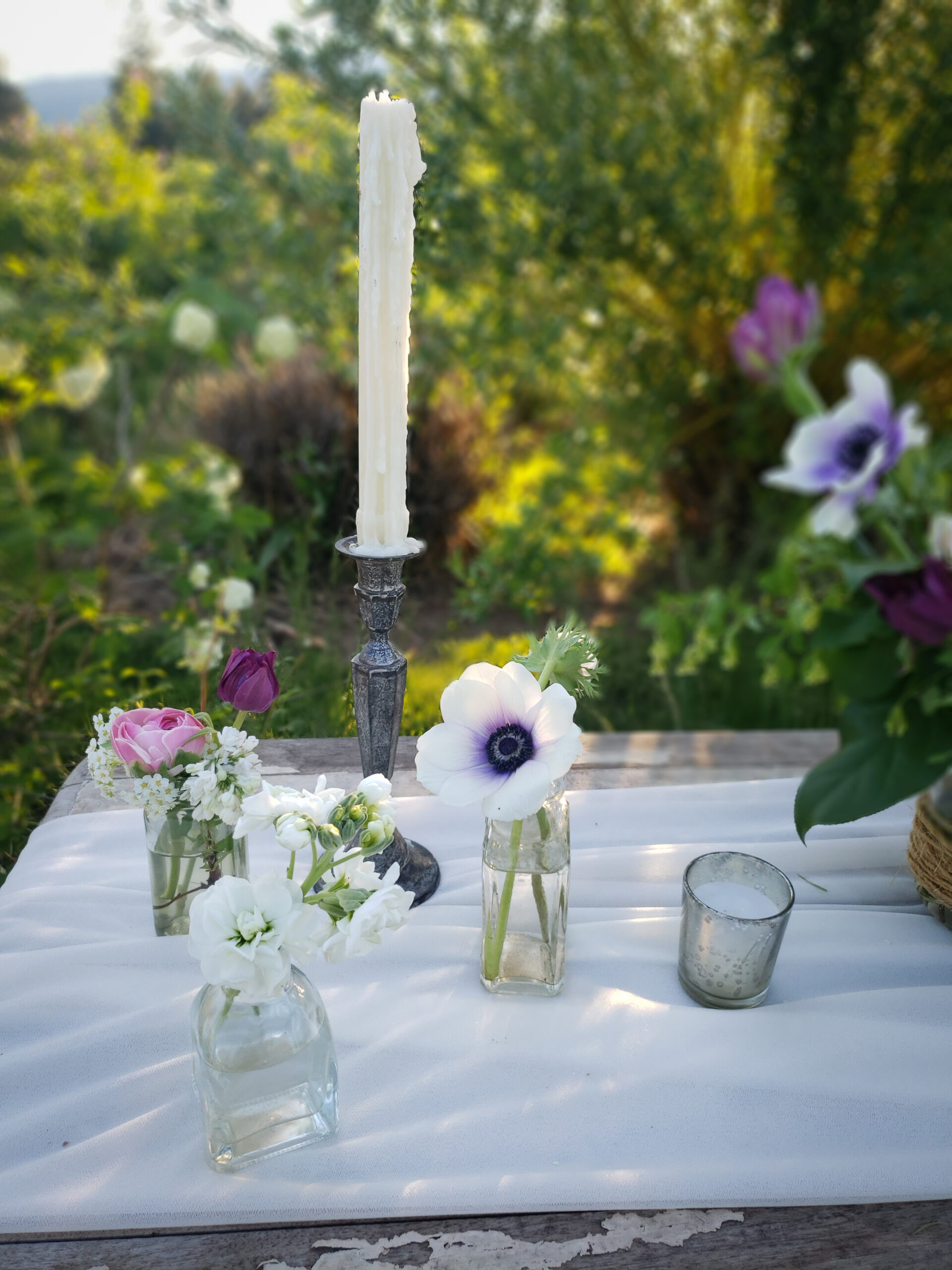 Three bottles on a table with a few flowers in them.