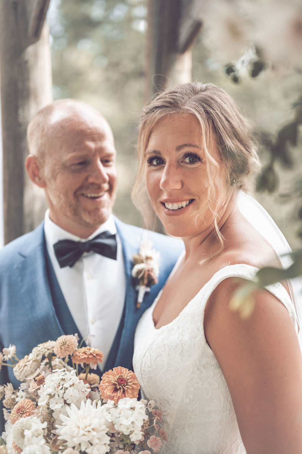 A happy couple getting married and the bride is looking at the camera and the groom is looking at the bride.