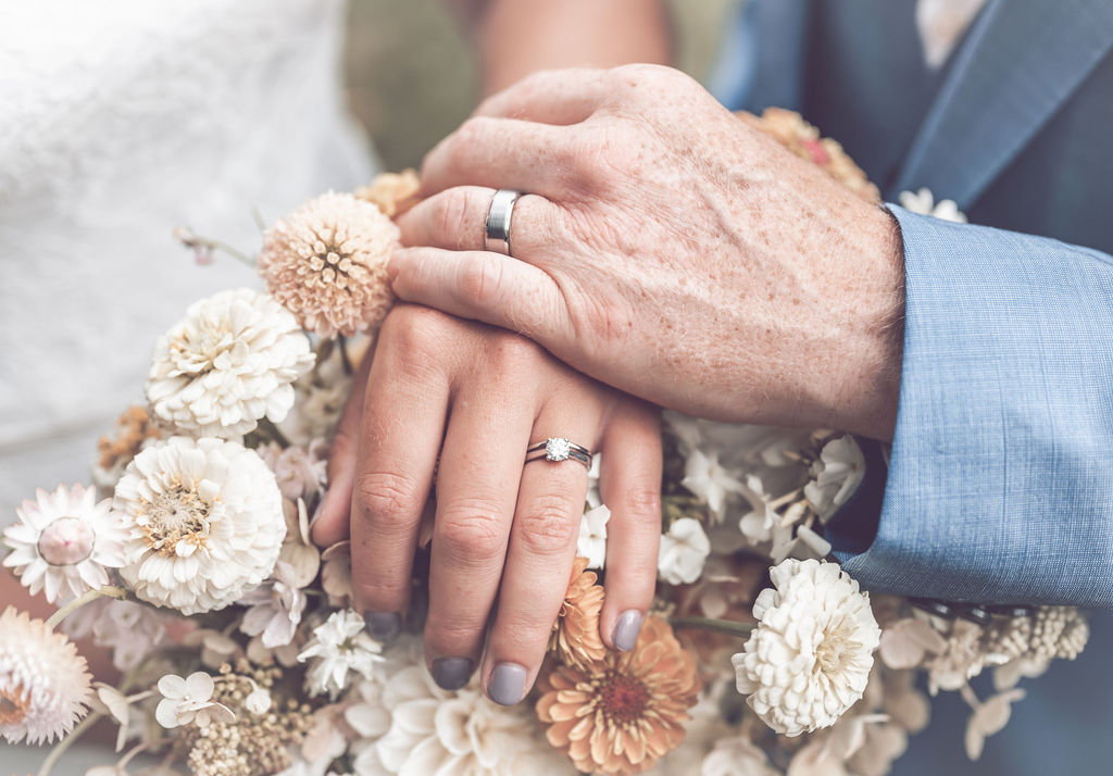 Bride and grooms hands with rings over a peach bridal bouquet